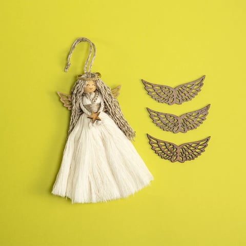 Adorno de ángel con vestido de flecos blanco y tres amuletos decorativos de alas sobre fondo amarillo