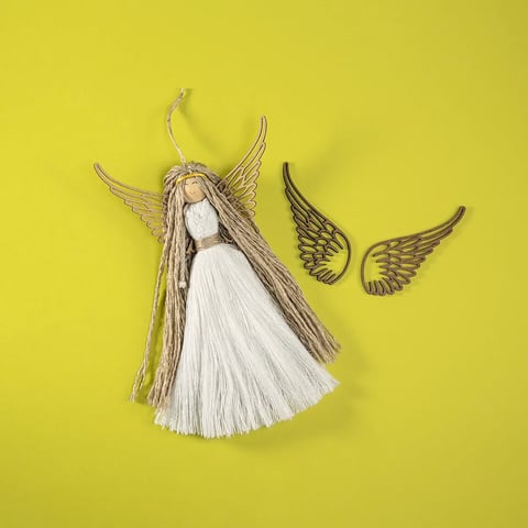 Figurita de ángel hecha a mano con falda blanca, alas doradas y cabello marrón sobre fondo amarillo con dos alas doradas junto a ella
