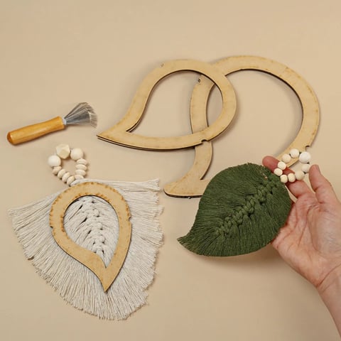 Colección de artículos artesanales de madera y tejidos hechos a mano incluyendo joyería de cuentas, piezas tejidas en forma de hoja con flecos y guirnalda decorativa sobre fondo neutro